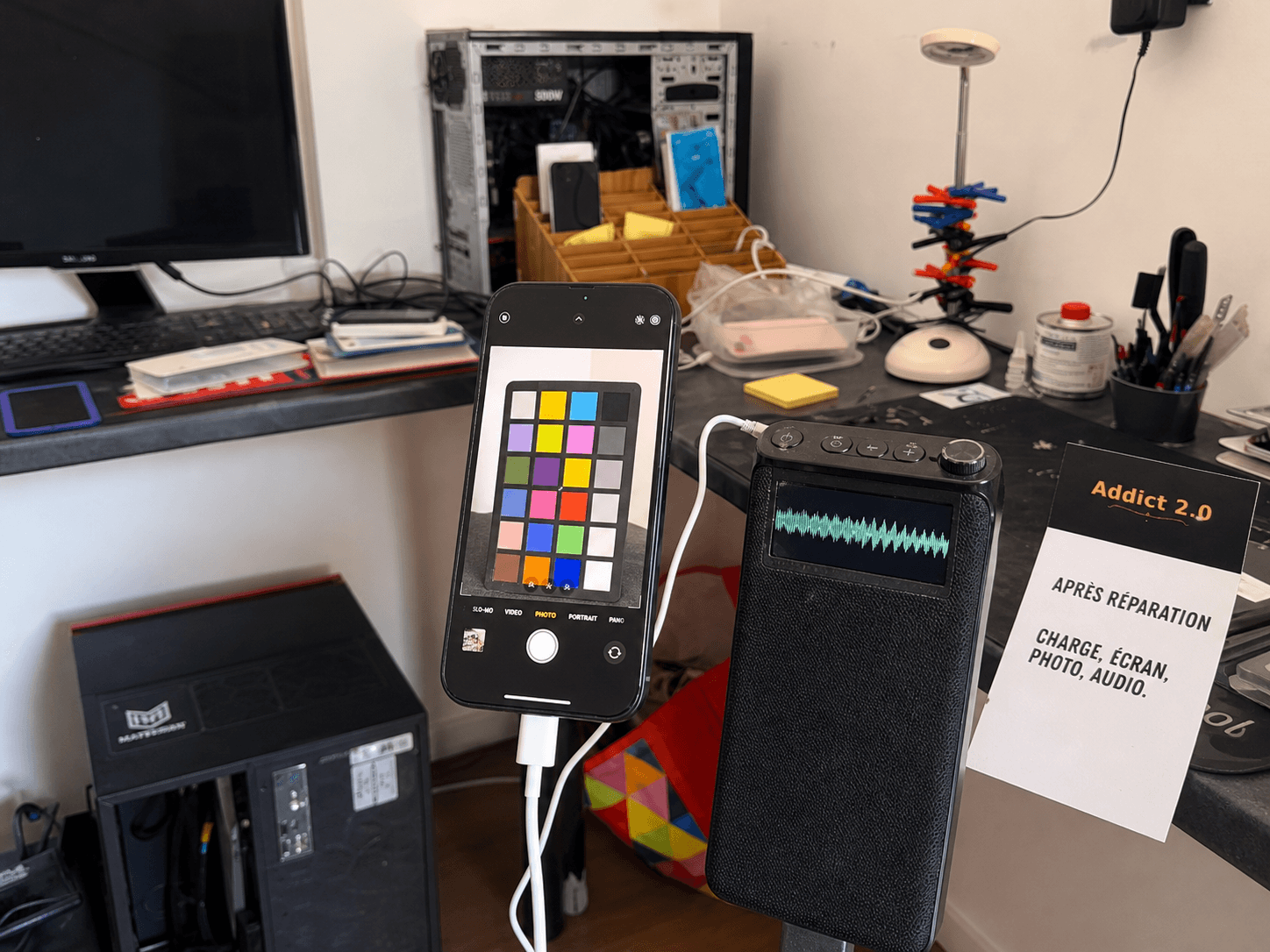 Dans le vrai atelier Addict 2.0, un téléphone générique est en charge et photographie une cible colorée pendant qu’un haut-parleur de test est contrôlé.